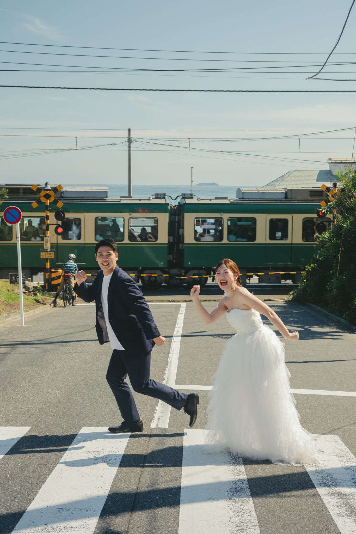 神奈川の江ノ島で海沿いの線路とレトロな電車を背景に踏切の横断歩道をポーズを決めて渡る映画のような前撮り