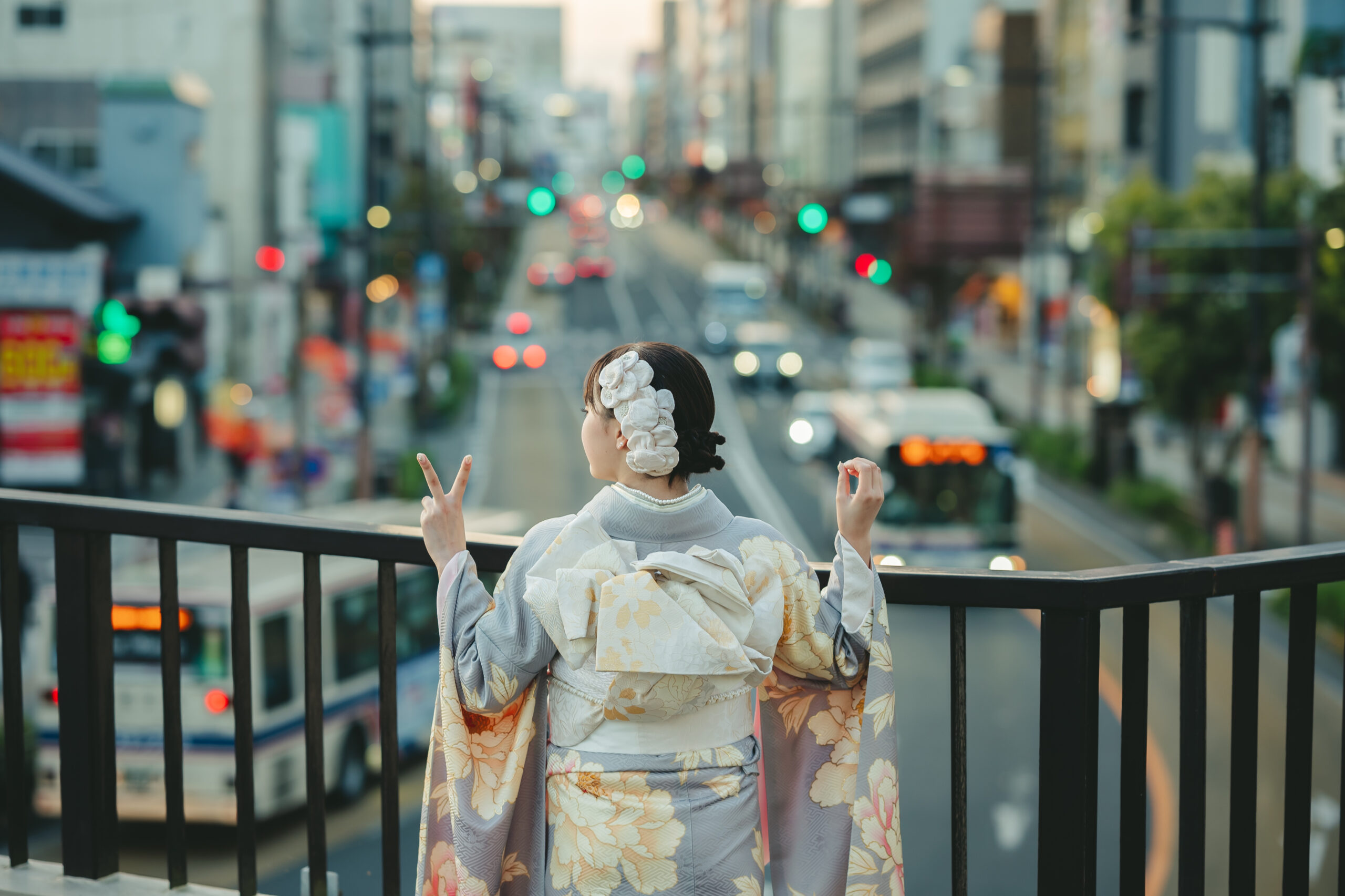 夕景の道路と街の灯りがエモく玉ボケする歩道橋の上で両手で20のポーズを作るドラマチックな成人式前撮り