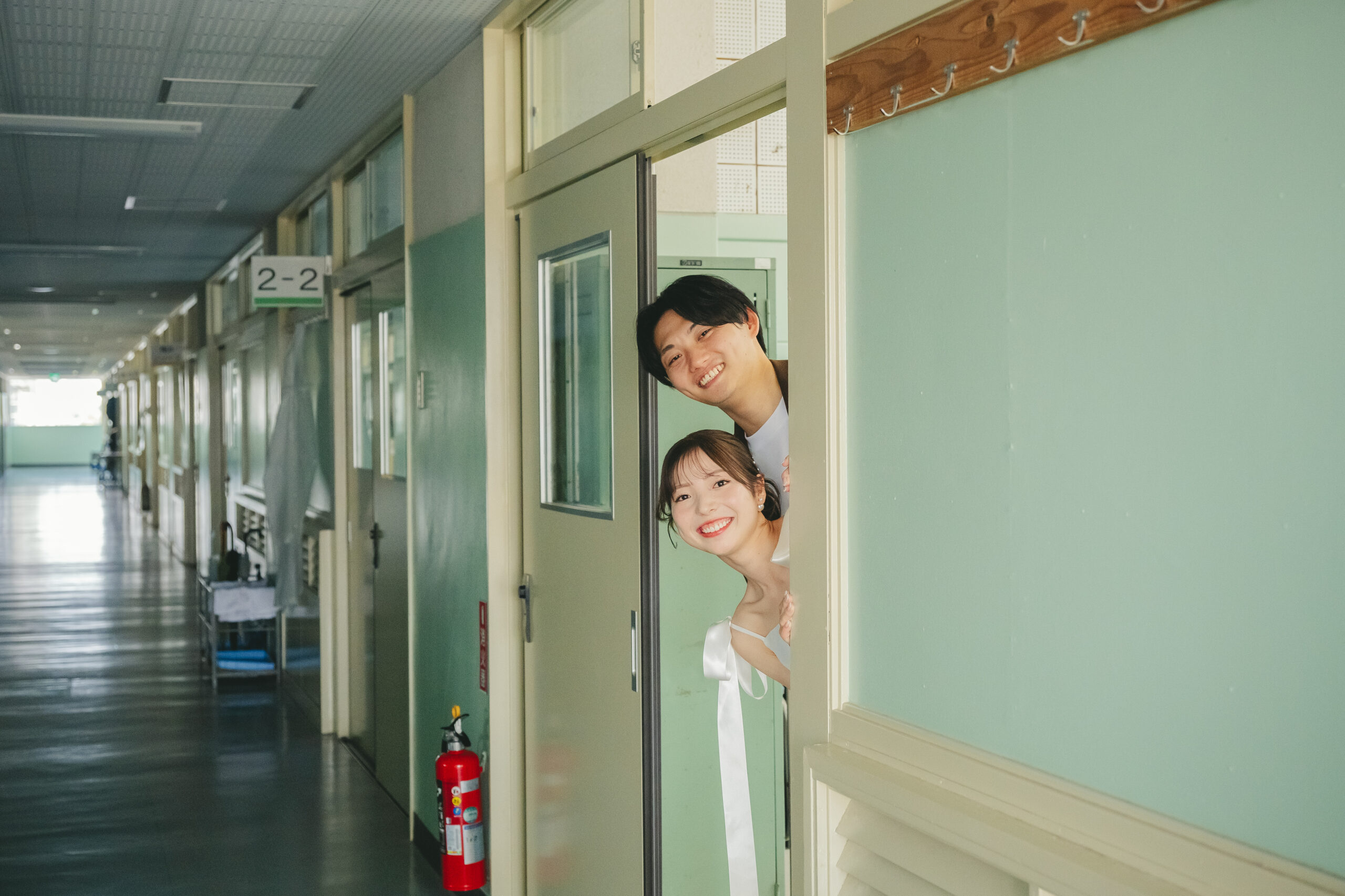 学校の教室のドアから二人でひょっこり顔を覗かせる楽しそうなウェディングフォト