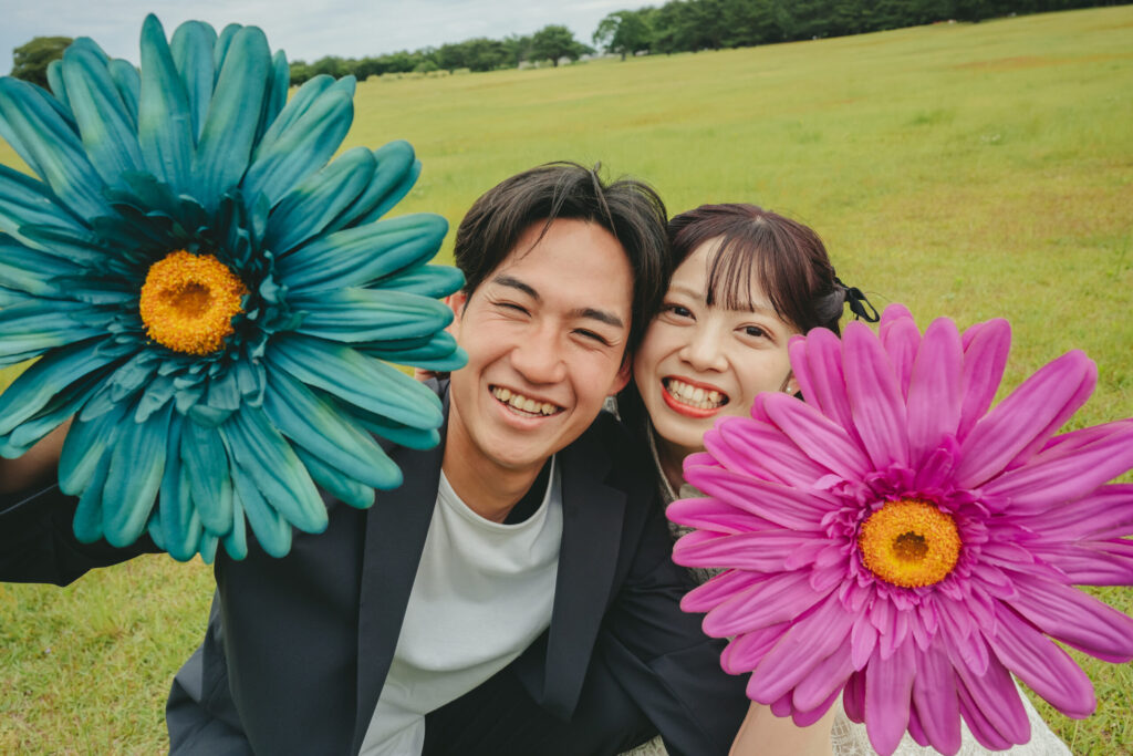国営ひたちなか海浜公園の美しい緑と芝生をバックにお花プロップスを持って笑うナチュラルな結婚式前撮り