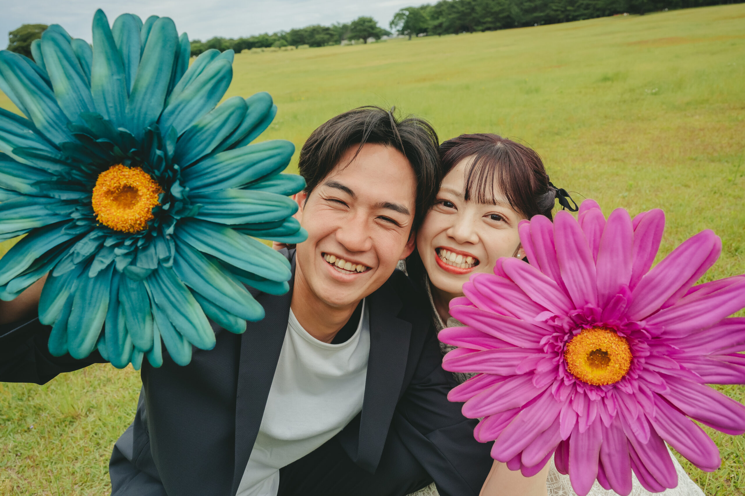 国営ひたちなか海浜公園の美しい緑と芝生をバックにお花プロップスを持って笑うナチュラルな結婚式前撮り