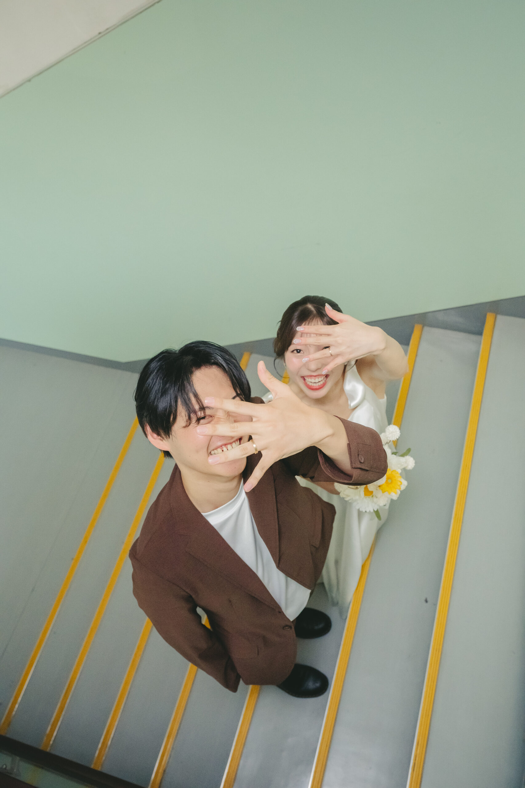 学校の階段でウエディングドレスとブラウンタキシード姿で並ぶノスタルジックな前撮り