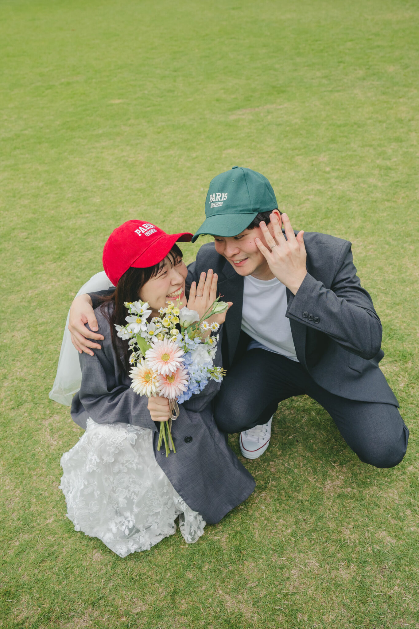 七ツ洞公園の綺麗な緑の芝生の上で仲良く並んでウエディングリングを見せる新郎新婦