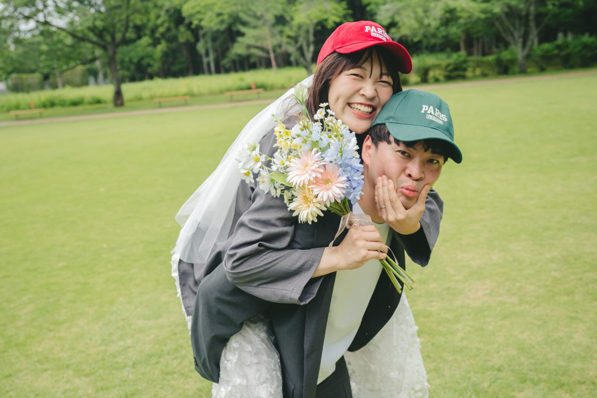 水戸市の七ツ洞公園の広い芝生でお揃いのキャップを被り笑顔でおんぶするナチュラルな前撮り