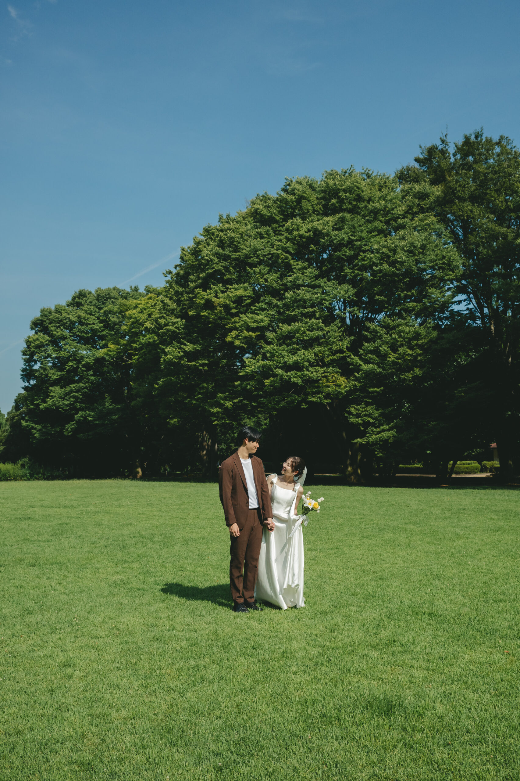 県立相模原公園の広大な芝生と青空の下で手を繋いで歩くナチュラルな結婚式前撮り