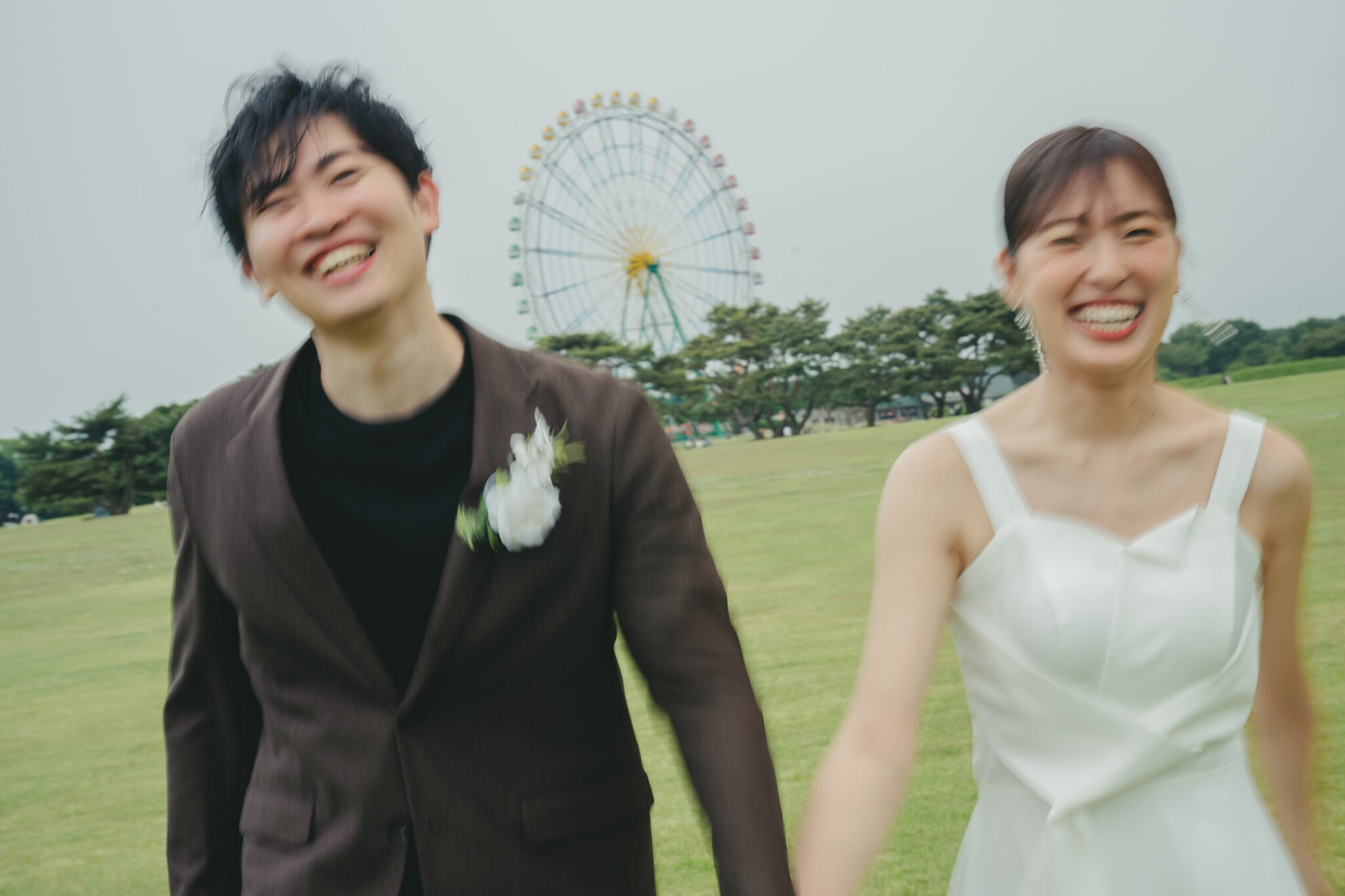 ひたちなか海浜公園の観覧車を背景に広い芝生の上を笑顔で駆け抜ける躍動感のあるウエディングフォト