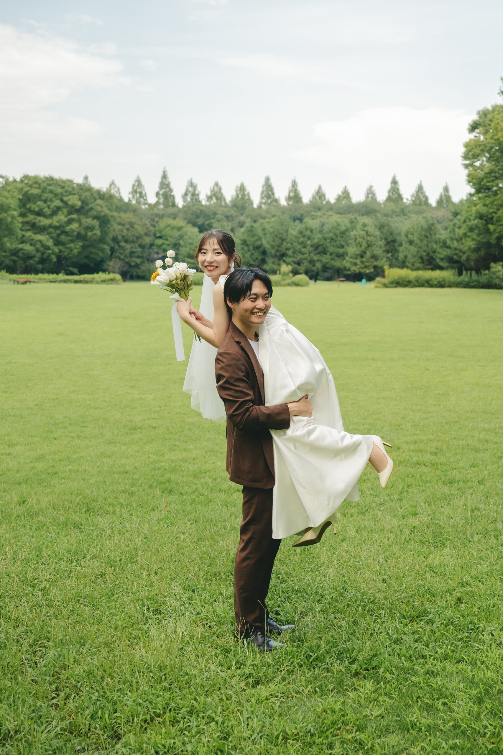 相模原公園の広い緑の中で新婦をお姫様抱っこして弾ける笑顔を見せるウエディングフォト