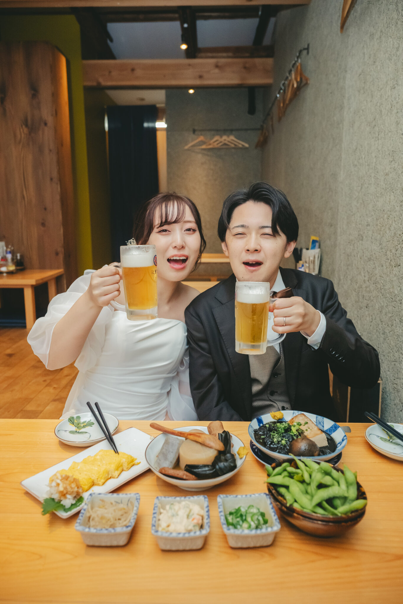 宇都宮駅近くの居酒屋カウンターでドレスとタキシード姿のまま生ビールで乾杯するおもしろ前撮り