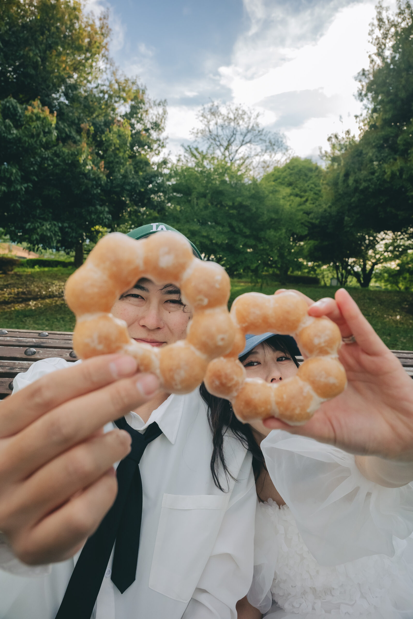 公園のベンチに座ってドーナツを美味しそうに頬張る可愛すぎるカジュアルウエディングフォト