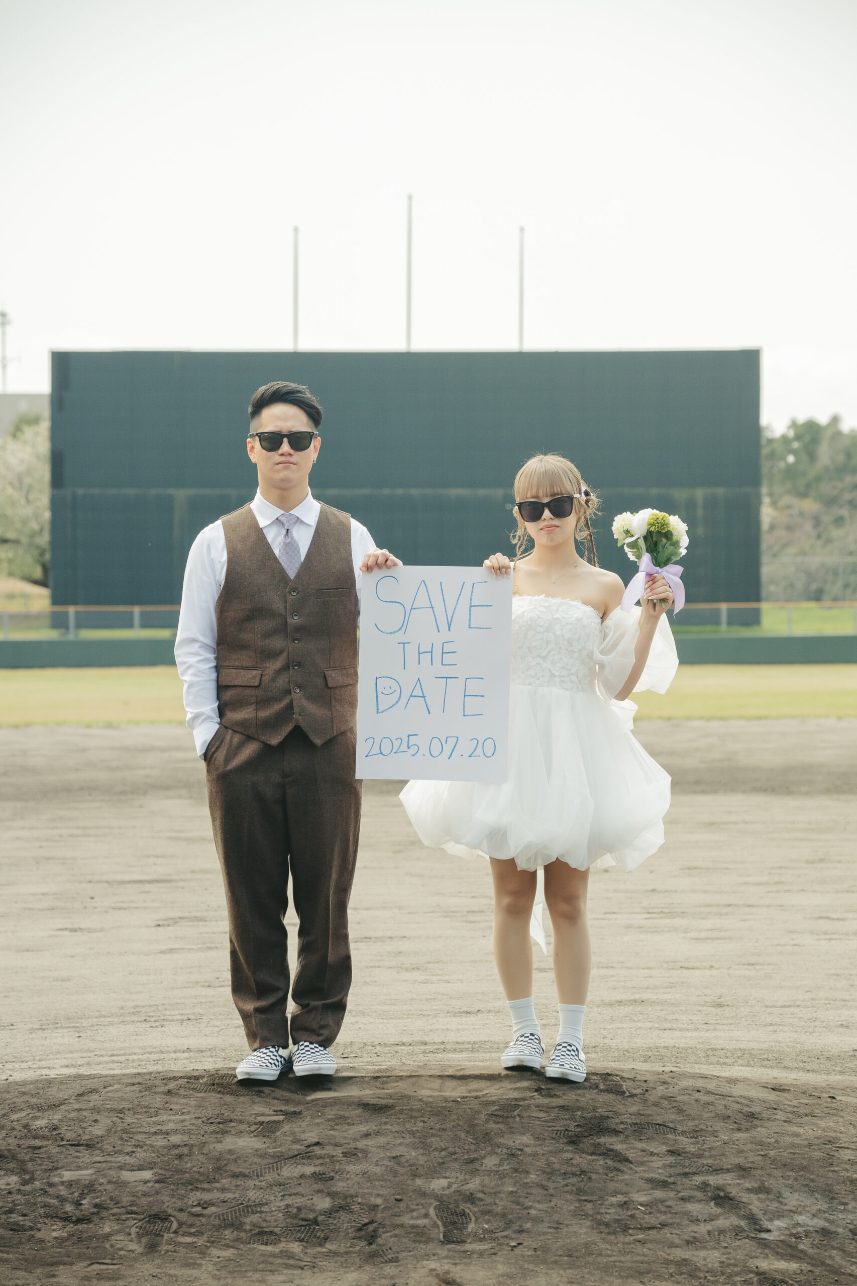 鹿児島県志布志市の有明球場でSAVETHEDATEのボードを持ちサングラスで前撮りをする二人