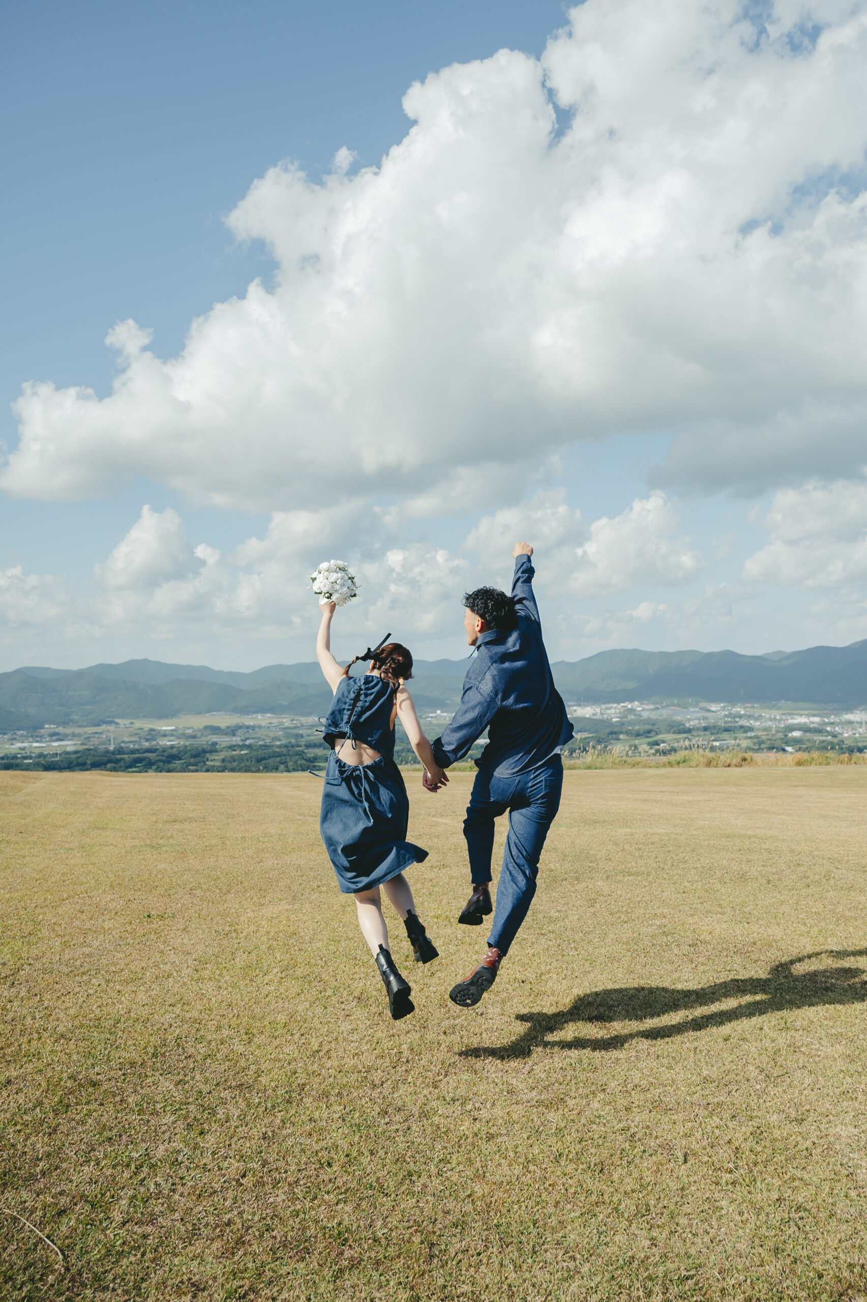 長崎県鬼岳の緑豊かな芝生と大パノラマを背景にデニムコーデで前撮りする二人