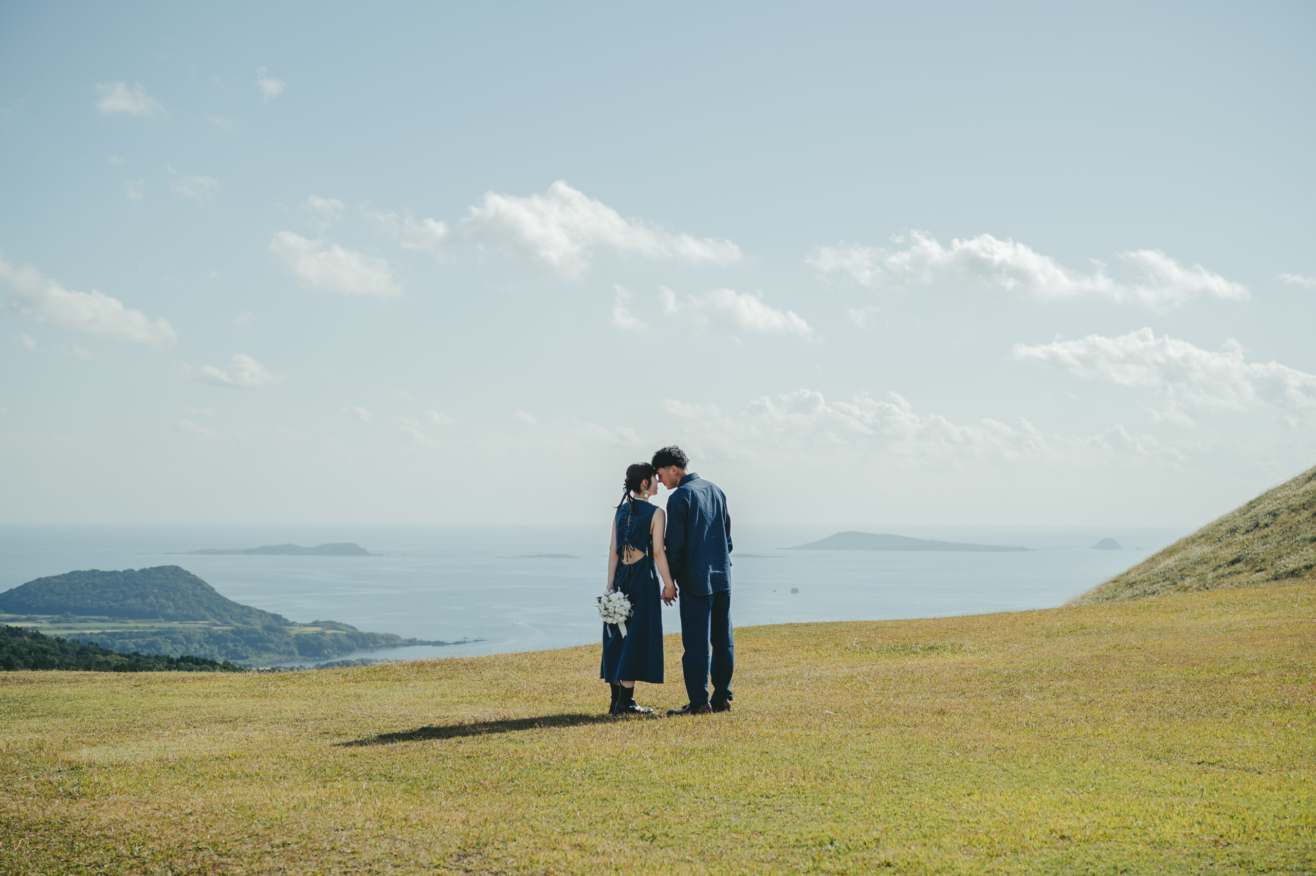 長崎県鬼岳の緑豊かな芝生と大パノラマを背景にデニムコーデで前撮りする二人