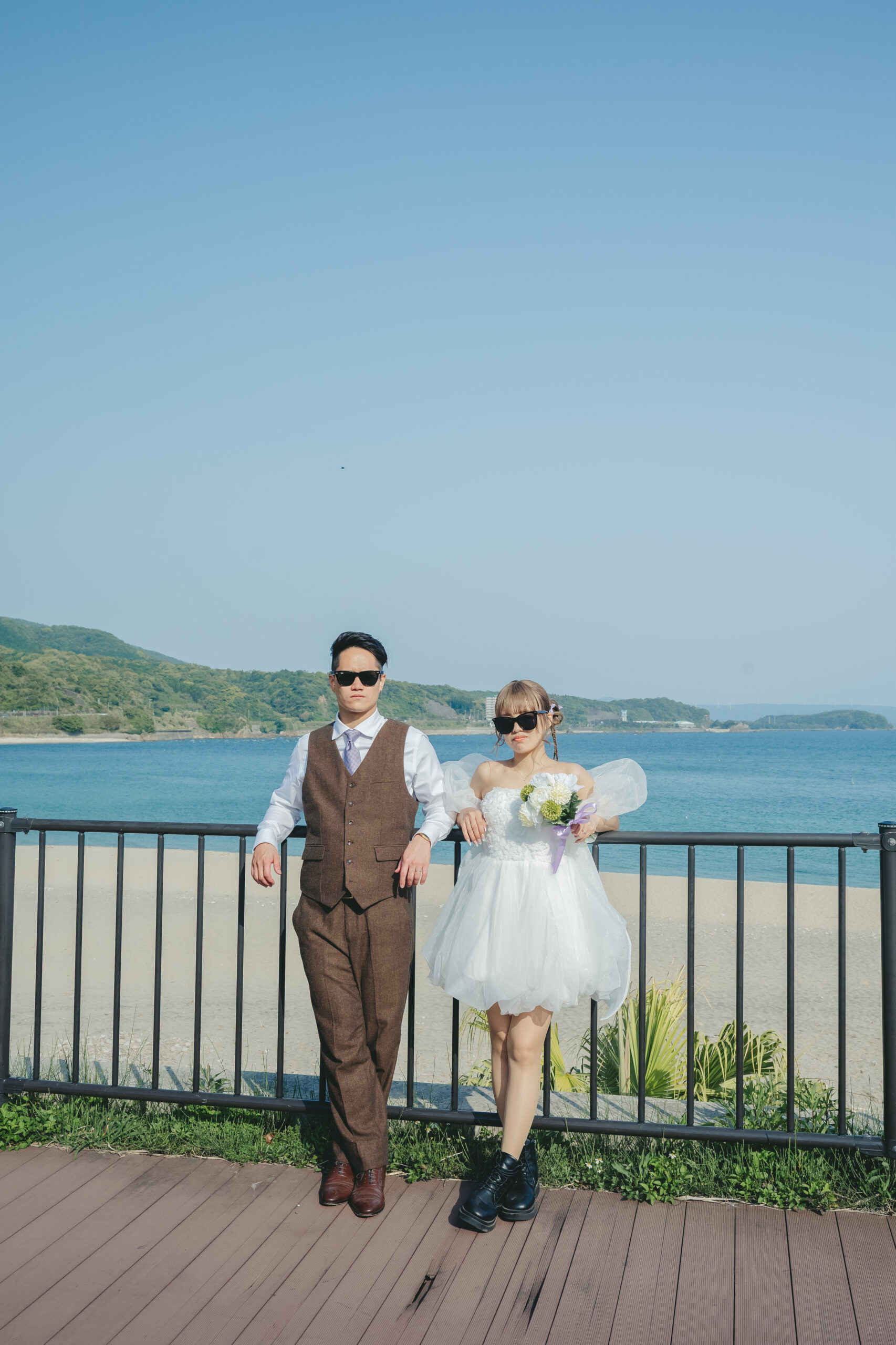 鹿児島のダグリ岬海岸で青い海を背景にサングラスをかけてポーズを決める前撮りカップル